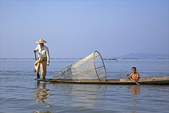 Intha fisherman steering traditional fishing boat by wrapping his leg around the oar, Inle Lake,