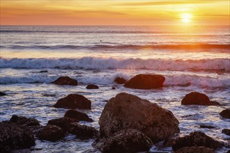 Atlantic ocean sunset with waves and rocks and surfers silhouettes in water at Costa da Caparica,