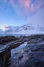 Beach of Norwegian sea on rocky coast in fjord on sunset in winter. Vareid beach, Lofoten islands,