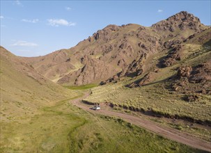 Aerial view, off-road vehicle on gravel road through a mountain valley, Naryn region, Kyrgyzstan,