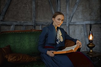 Attractive lady in oldfashioned clothes reading ancient book near vintage kerosene lamp