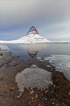 Kirkjufell, nunatak hill covered in snow reflected in water of fjord on the Snæfellsnes peninsula