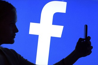 Silhouette of a woman with a smartphone in her hand in front of a Facebook logo, 12/01/2016