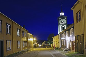 Street view of a traditional town at night with illuminated old buildings and a church tower,