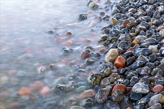 Blurred sea water of wave rolling over wet colourful pebbles on shingle beach, cobble beach