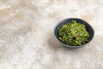 Chuka seaweed salad in blue ceramic bowl on brown concrete background. Side view, copy space