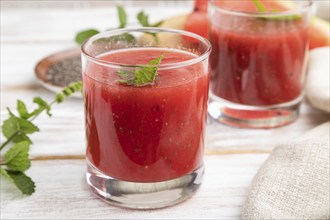 Watermelon juice with chia seeds and mint in glass on a white wooden background with linen textile.