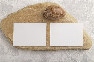 White paper business card, mockup with natural stone and seashell on gray concrete background.