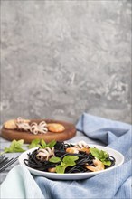 Black cuttlefish ink pasta with shrimps or prawns and small octopuses on gray wooden background and