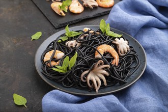 Black cuttlefish ink pasta with shrimps or prawns and small octopuses on black concrete background