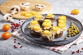 Stuffed fried champignons with cheese, kumquats and green peas on a gray concrete background.