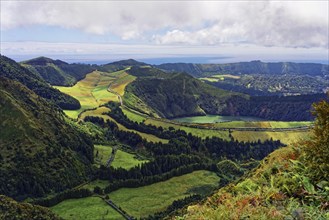 Panorama of the green framed crater lake Lagoa de Santrago amidst hilly terrain and cloudy skies,