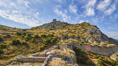 Ancient fortress ruins on a mountain with blue sky and visible path through the grounds, Archaic