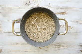 Overhead view of beans soaking in a casserole of water. White beans in water in a pot