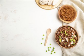 Quinoa porridge with green pea and chicken in wooden bowl on a white wooden background and linen