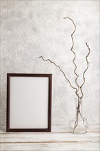 Brown wooden frame mockup with dried wine branch in glass on gray concrete background. Blank,