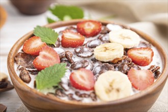 Chocolate cornflakes with milk and strawberry in wooden bowl on white wooden background and linen