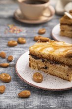 Honey cake with milk cream, caramel, almonds and a cup of coffee on a gray wooden background and