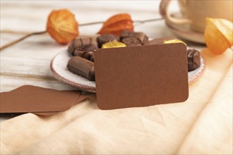 Brown business card with chocolate candies and physalis flowers on a white wooden background and