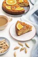 Orange cake with almonds and a cup of coffee on a white concrete background and blue linen textile.