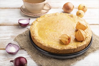 Autumn onion pie and cup of coffee on white wooden background and linen textile. Side view, close