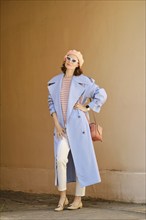 Trendy woman in long blue trench coat posing outdoors