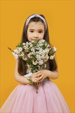 Cute young girl with bouquet of spring flowers over yellow background