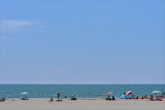 Beach with people and colourful parasols in front of a wide, blue Mediterranean Sea under a clear