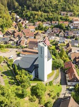 Village with a church and a striking clock tower, surrounded by green countryside and hilly nature,