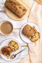 Homemade cake with raisins, almonds, soft caramel and a cup of coffee on a white wooden background