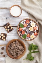 Chocolate cornflakes with milk and strawberry in wooden bowl on white wooden background and linen