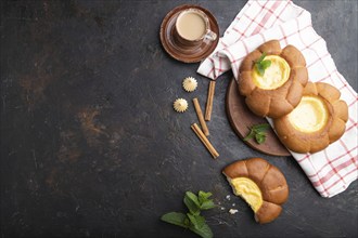 Sour cream bun with cup of coffee on a black concrete background and linen textile. top view, flat