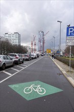 View of a car park with cycle path and high-rise buildings and construction cranes in the