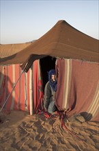 Model Released Young tourist boy dressed with blue nomad head scarf kneels at the entrance to a