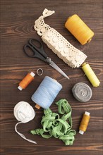 Sewing accessories: scissors, thread, thimbles, braid on brown wooden background. Top view, flat