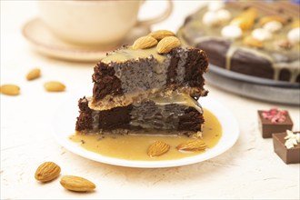 Pieces of chocolate brownie cake with caramel cream and almonds on a white concrete background.