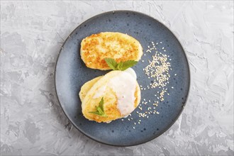 Cheese pancakes on a blue ceramic plate with milk sauce on a gray concrete background. top view,