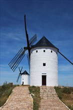 Two white windmills stand under a clear blue sky, embedded in a natural summer landscape, Alcazar