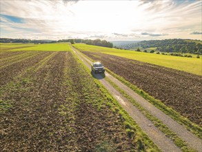 A car drives along a rural road, surrounded by expansive fields under bright daylight, car sharing,