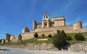 Medieval castle with towers and stone walls under a blue sky, surrounded by green spaces, Turégano,