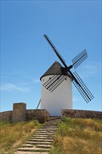 A historic windmill with black wings stands under a clear blue sky, surrounded by grassy hills and