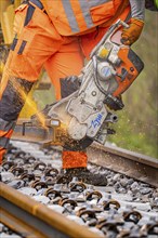 A construction worker uses a chainsaw to cut a track while sparks fly, track construction, Hermann