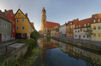 The morning sun illuminates a picturesque street along the river Vils and the church tower of St