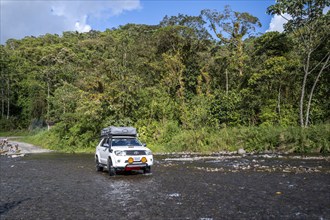 Toyota off-road vehicle with roof tent drives through a wide river in the rainforest, Alajuela