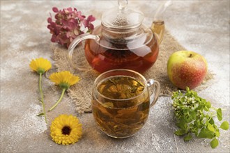 Red tea with herbs in glass teapot on brown concrete background and linen textile. Healthy drink