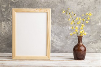 Wooden frame with yellow barrenwort flowers in ceramic vase on gray concrete background. side view,