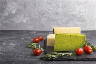 Green basil cheese and various types of cheese with rosemary and tomatoes on black slate board on a