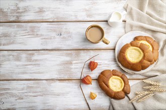 Sour cream bun with cup of coffee on a white wooden background and linen textile. top view, flat