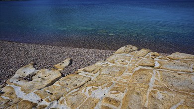 Rocky coast with pebbles and clear blue water under a blue sky, Lambi beach, pebble beach, Patmos,