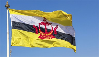 The flag of Brunei flutters in the wind, isolated against a blue sky